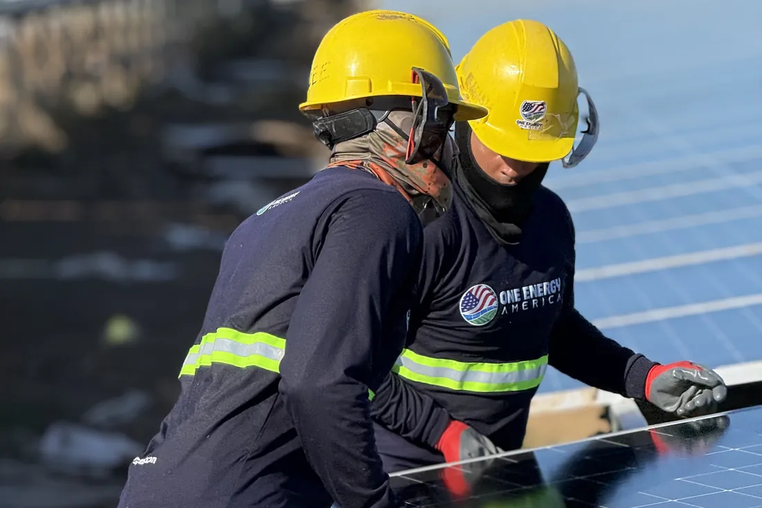 Two One Energy America installers setting a solar module on a tracker